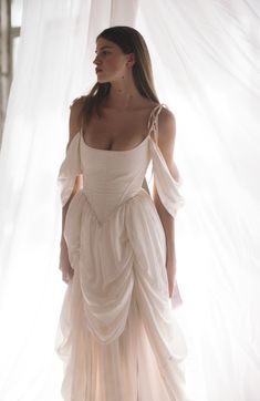 a woman standing in front of a white curtain wearing a dress with ruffles