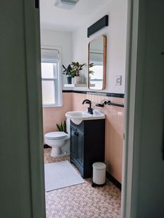 a bathroom with pink and black tile flooring next to a white toilet sitting under a window