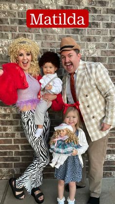 a man and two women posing for a photo with their doll babies in front of a brick wall