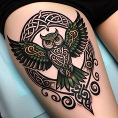 an owl tattoo on the thigh with celtic patterns and swirls around it's wings