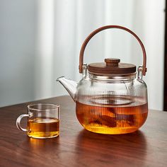 a glass tea pot with a wooden lid and handle next to a cup of tea