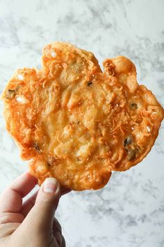 a person holding up a fried food item in their hand on a marble countertop