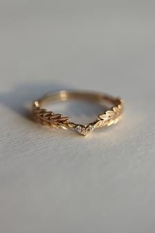 a gold wedding band with leaves on the side and a diamond in the middle, sitting on a white surface