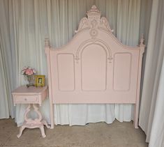 there is a pink bed and a small table in front of the curtained wall