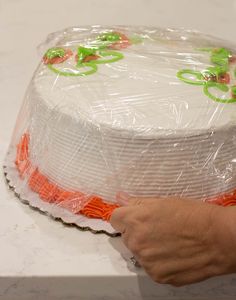 a cake wrapped in plastic and sitting on a counter top with someone's hand reaching for it