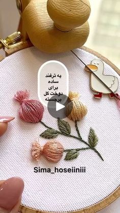 someone is stitching flowers on a wooden hoop with needle and thread in front of them