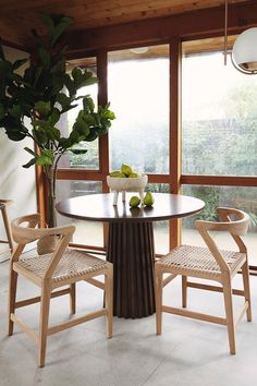 a dining room table with two chairs and a vase filled with fruit on top of it