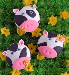 three cupcakes decorated like cows with flowers in the grass and daisies around them