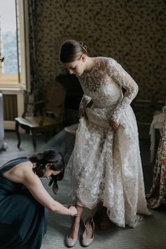 two women in dresses and one is bending down to pick up something from the floor