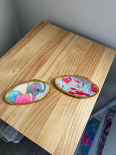 two decorative plates sitting on top of a wooden table next to each other in front of a white wall