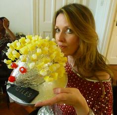 a woman is holding a vase with flowers in it and looking at the camera while another person sits behind her