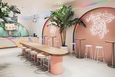 the interior of a restaurant with pink walls and wooden benches, palm trees, and neon lights