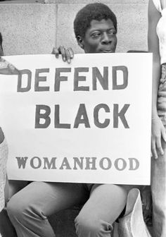 two women holding a sign that says defend black womanhood