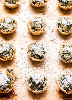 several mini pizzas with spinach and cheese on top sitting on a baking sheet