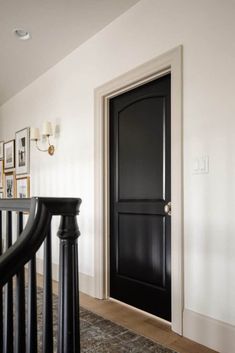 a black door is on the side of a white wall next to a banister