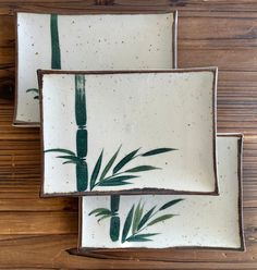 two white plates with green bamboo designs on them sitting on a wooden table next to each other