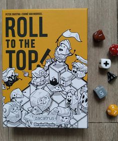 the book roll to the top is surrounded by dices and other toys on a wooden surface