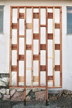 a wooden trellis on the side of a white building next to a rock wall