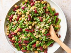 a white bowl filled with green beans and other food items next to a wooden spoon