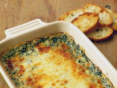 a casserole dish with spinach, cheese and bread slices on the side