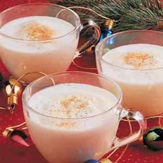 three glasses filled with white liquid on top of a red tablecloth next to christmas decorations