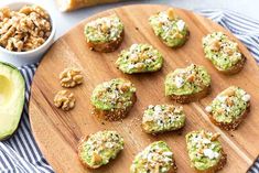 a wooden plate topped with mini sandwiches next to an avocado and walnuts