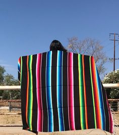 a person sitting on a bench wrapped in a colorful blanket with their back to the camera