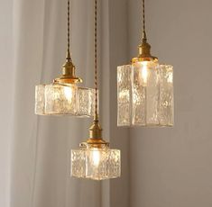 three light fixtures hanging from a ceiling in a room with white walls and flowers on the table