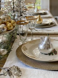 a table set for christmas with silver and gold ornaments on the placemats, glassware, and plates