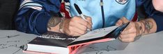 a man signing autographs for fans at a table with books and pens on it