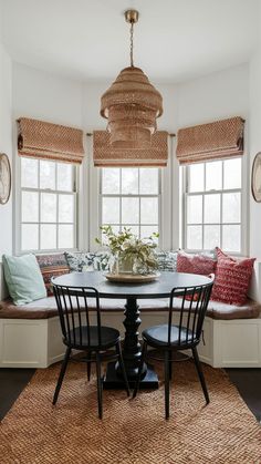 a dining room table with four chairs and a bench in front of two windows that have matching cushions on them