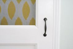 a door handle on a white door with a yellow and gray wallpaper behind it