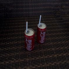 two soda cans with straws in them sitting on the ground