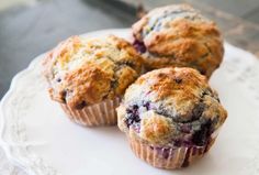 three blueberry muffins sitting on top of a white plate next to each other