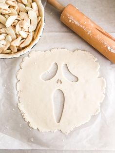 an uncooked pizza dough next to a rolling pin and bowl of sliced almonds