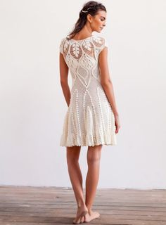 a woman in a short white dress standing on a wooden floor with her back to the camera