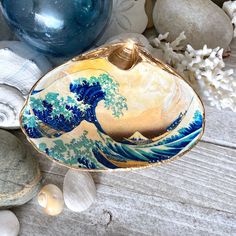 a bowl with an ocean wave painted on it sitting next to rocks and seashells