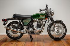 a green and black motorcycle parked on top of a hard wood floor next to a white wall