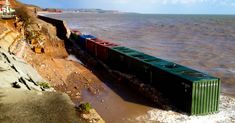 a cargo train traveling along the side of a cliff near the water's edge