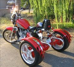 two red motorcycles parked next to each other on the street in front of some trees