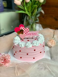 a pink cake sitting on top of a table with flowers in the vase behind it