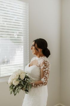 a woman standing in front of a window holding a bouquet