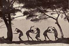 an old black and white photo of people doing yoga in front of the water with trees