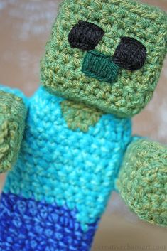 a crocheted green and blue teddy bear with black eyes, arms and legs