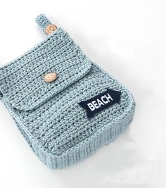 a blue crocheted pouch with a button on the side and a name tag attached to it