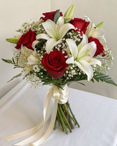 a bouquet of white lilies and red roses on top of a table with ribbon