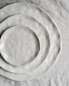 three white plates with speckles on them sitting on top of a table cloth