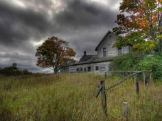 an old house sits in the middle of a field with tall grass and trees around it