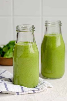 two jars filled with green smoothie sitting on top of a table