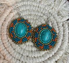 two pairs of earrings with turquoise and orange beads on top of a white piece of yarn